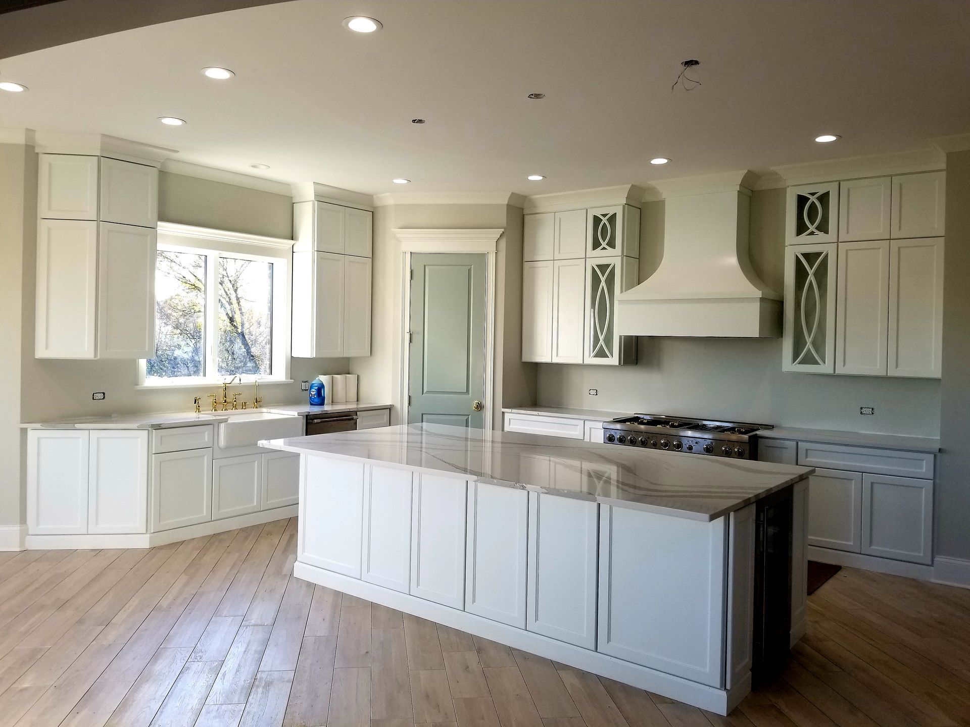 Bright modern kitchen with white cabinets, island, marble countertop, and wooden floors