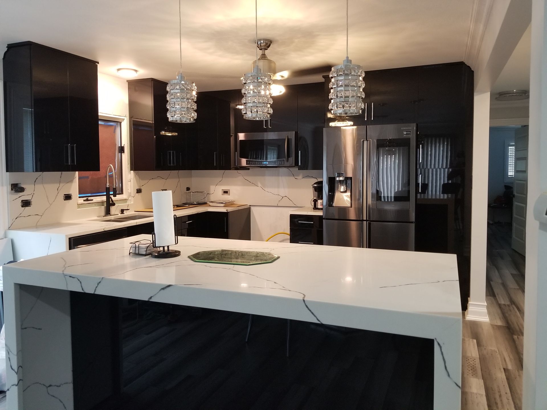 Modern kitchen with black cabinets, white island countertop, pendant lights, and stainless steel appliances