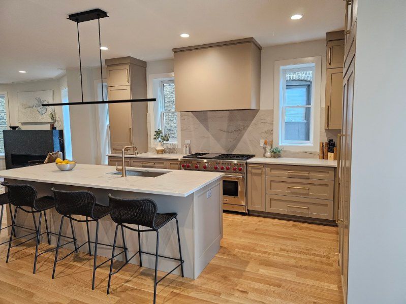 Modern kitchen with a large island, black stools, light wood cabinets, and stainless steel range hood