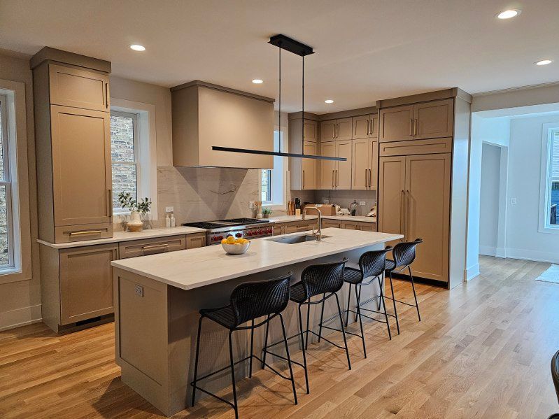 Modern kitchen with large island, bar stools, light wood floors, and pendant range hood