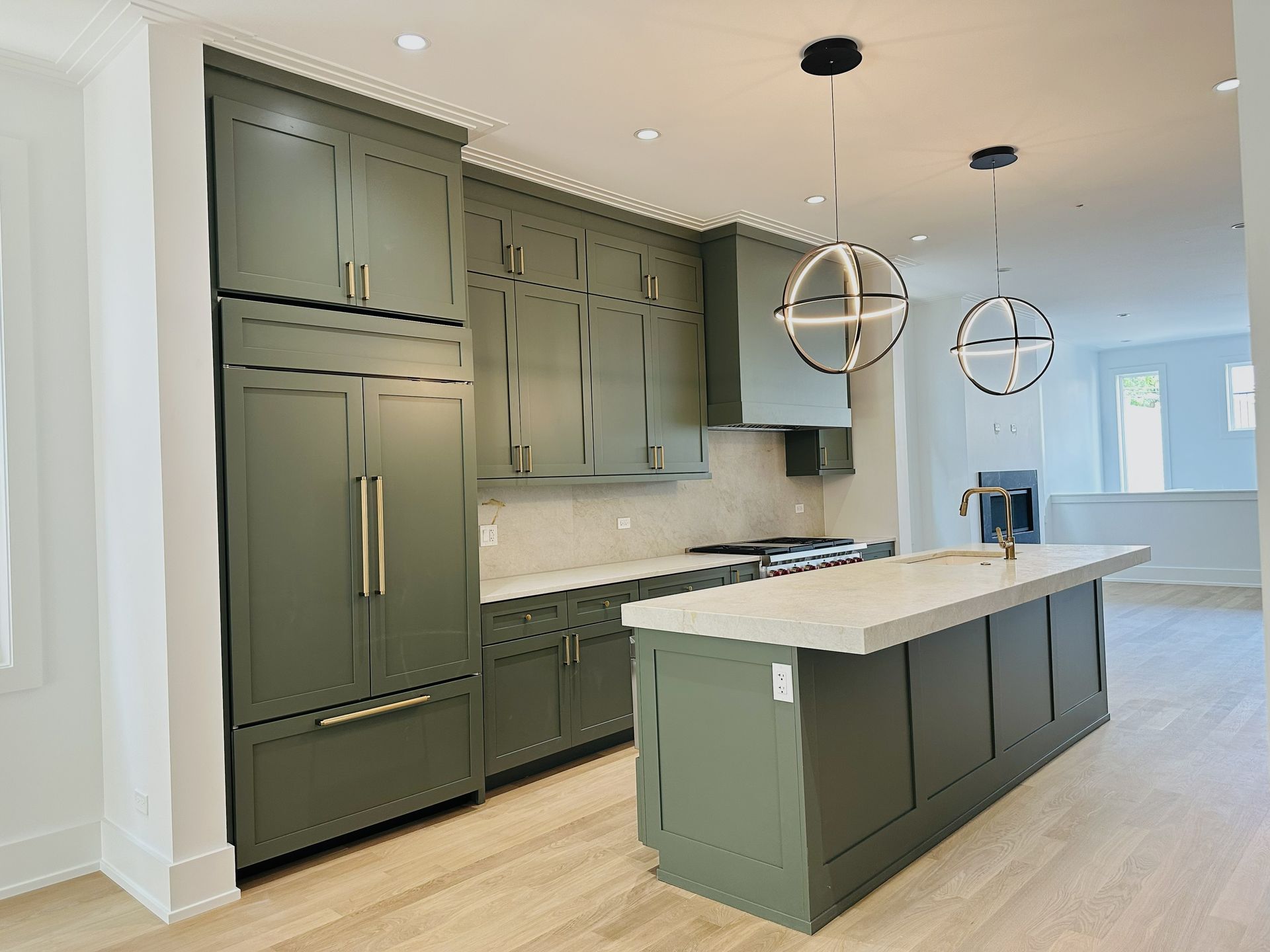 Modern kitchen with dark green cabinets, white island, pendant lights, and stainless appliances