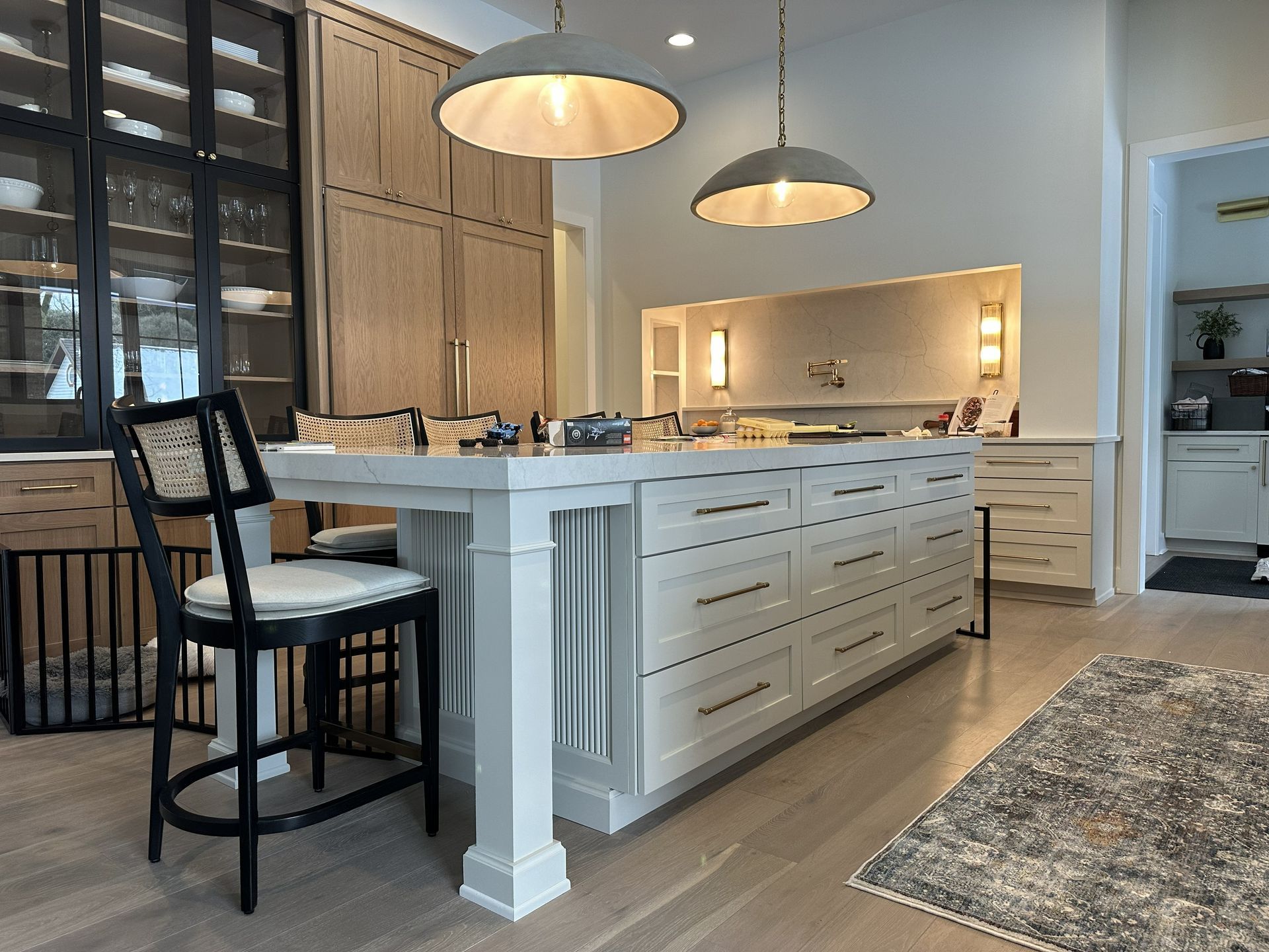 Modern white kitchen with island seating, pendant lights, and a large rug on wood floors