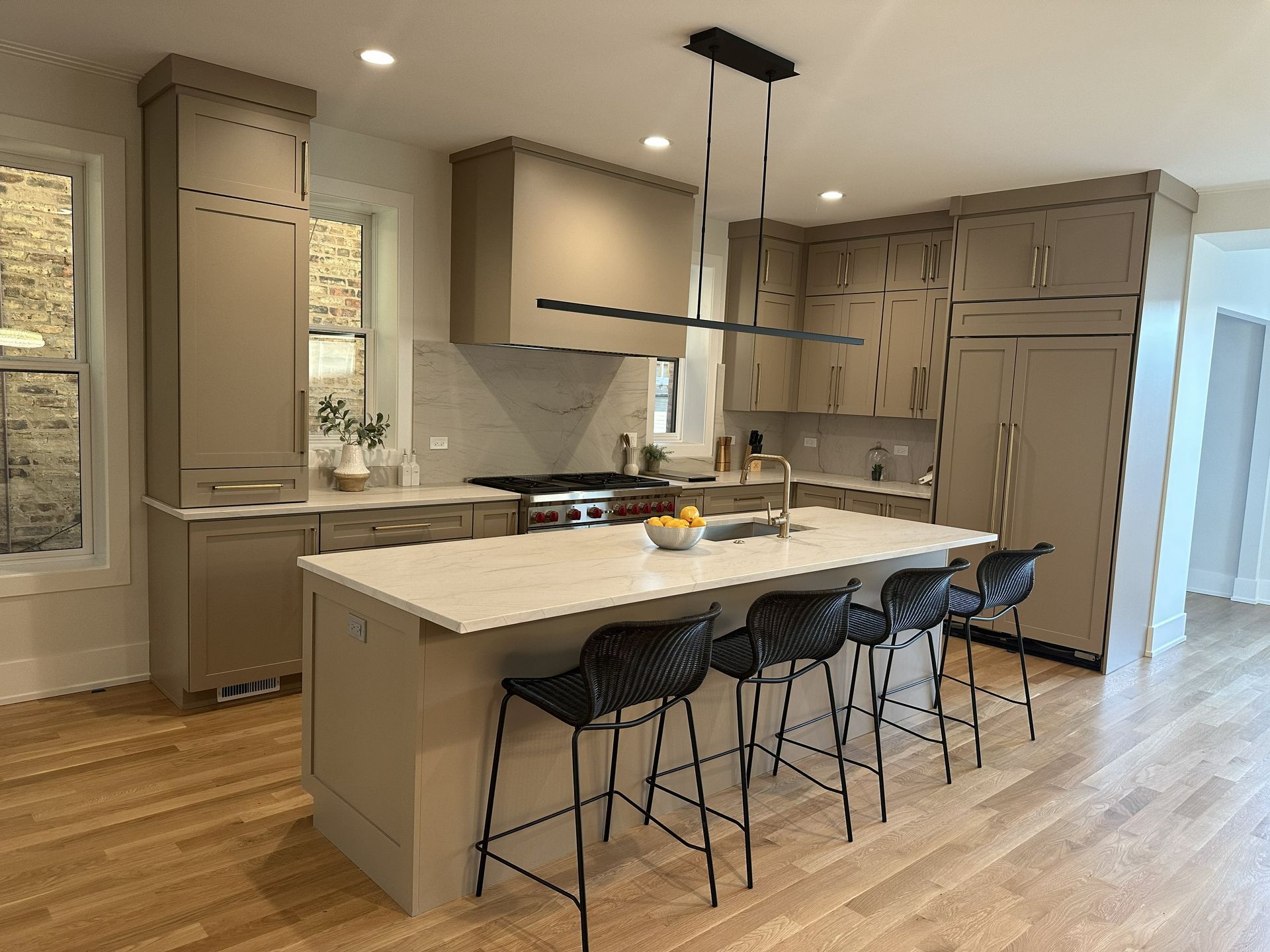 Modern kitchen with gray cabinets, large island, and four black barstools on a wood floor