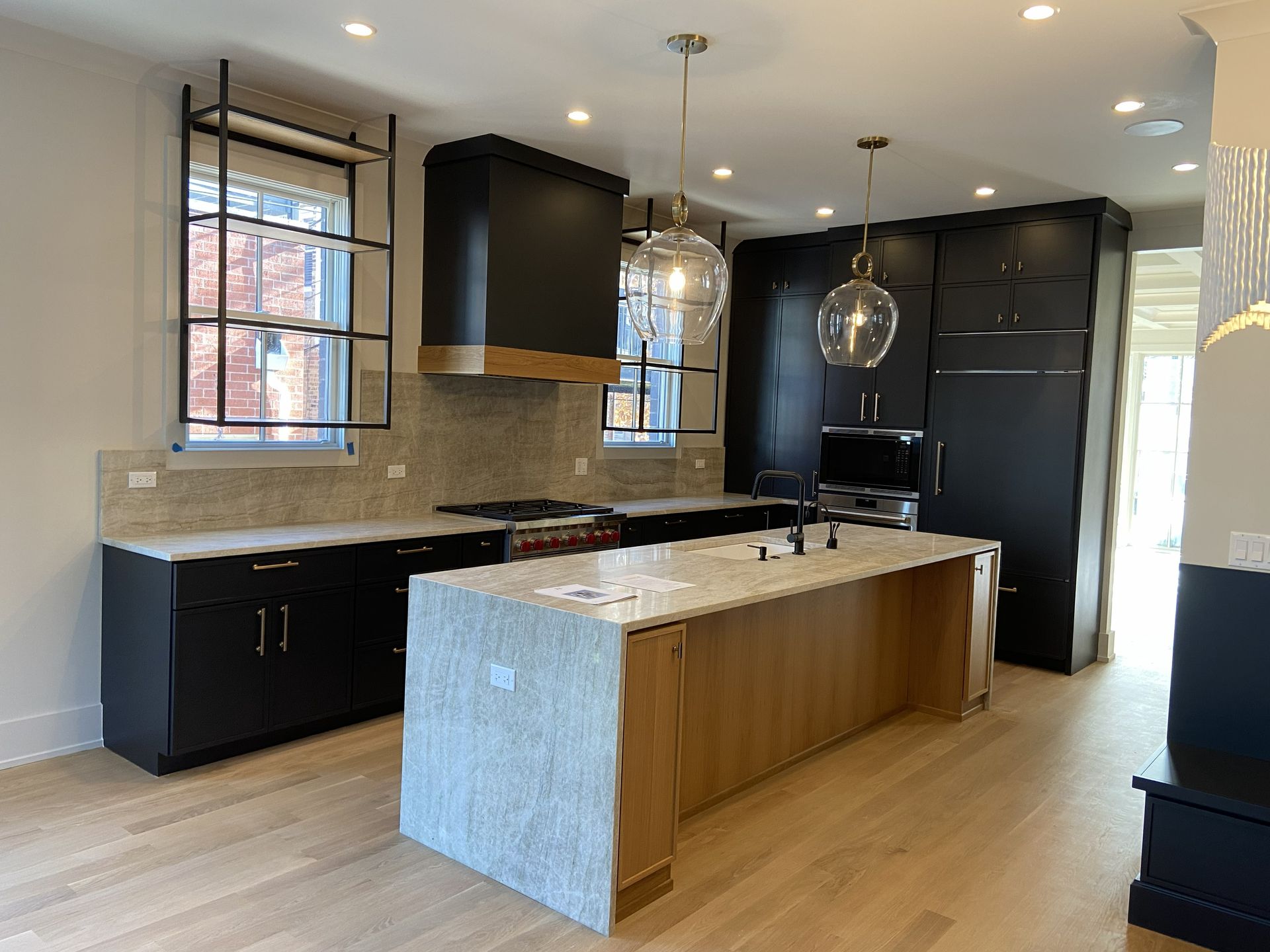 Modern kitchen with black cabinets, marble island, pendant lights, and large windows