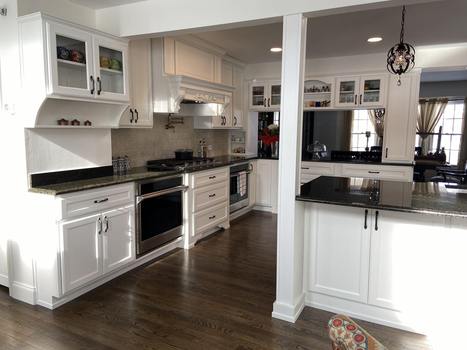 Bright white kitchen with black countertops, stainless appliances, and dark hardwood floors