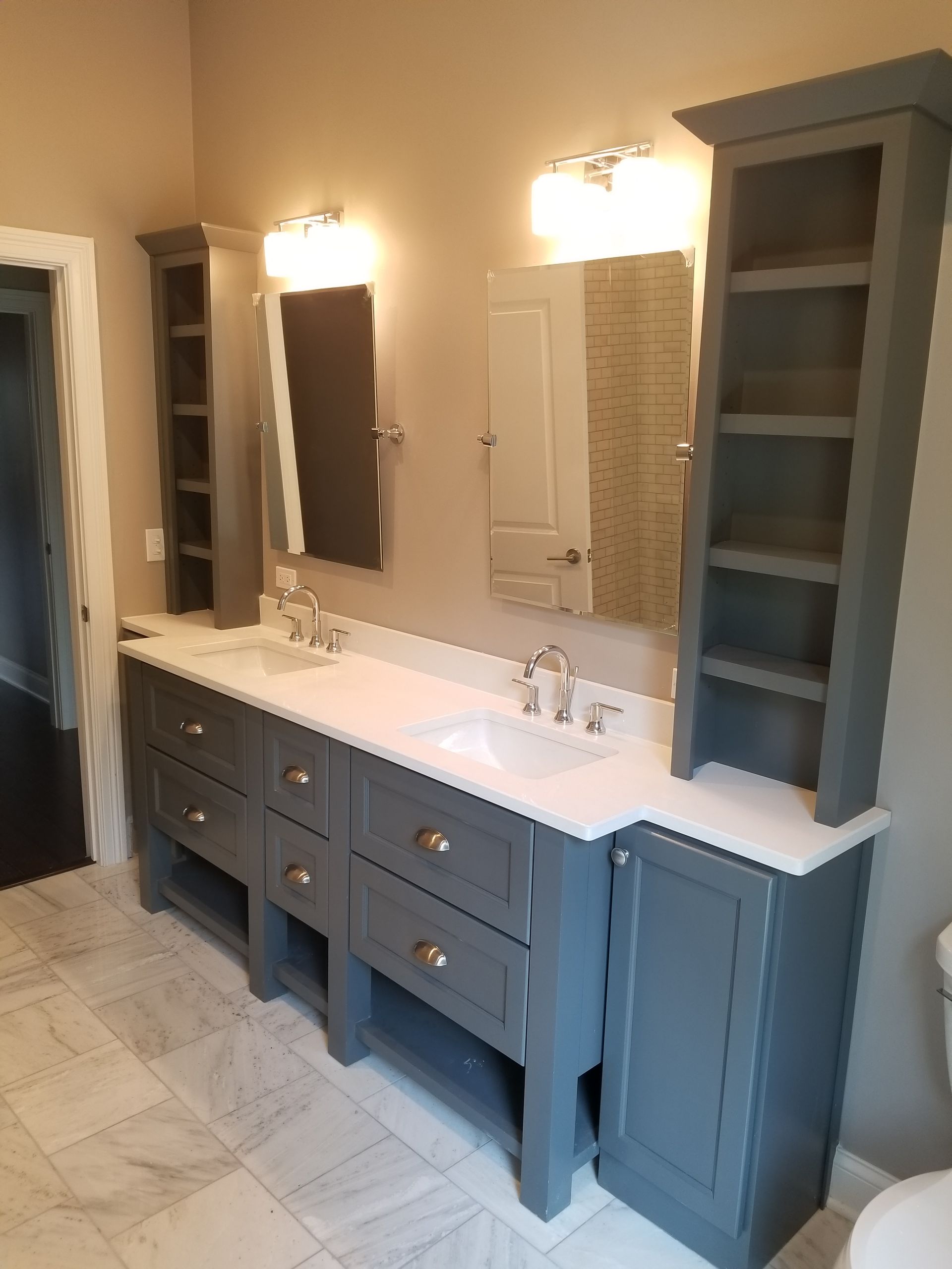 Blue double-sink bathroom vanity with mirrors, lights, and built-in storage cabinets against a tiled wall