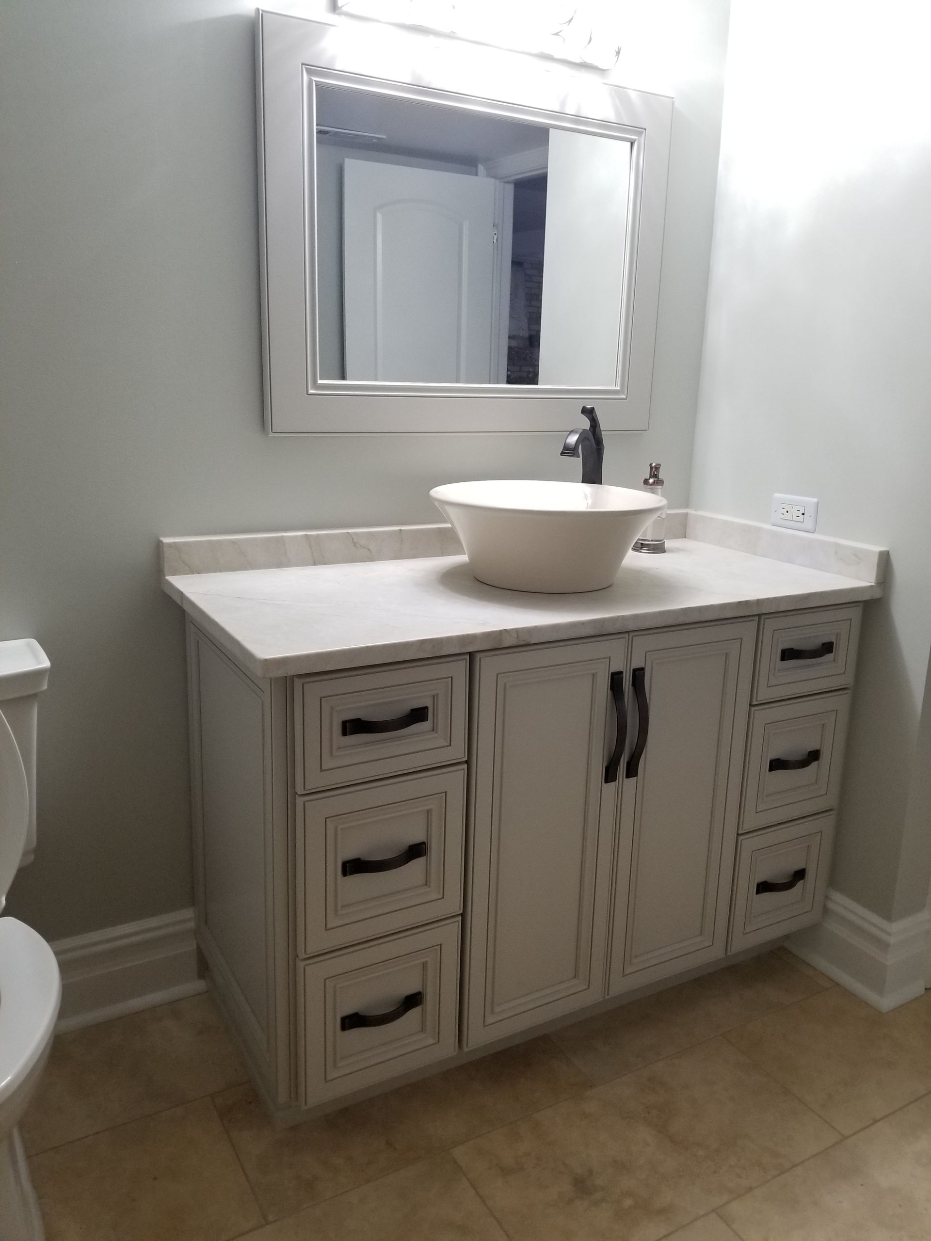 Bathroom vanity with white sink, mirror, and light wood cabinets on beige tile floor