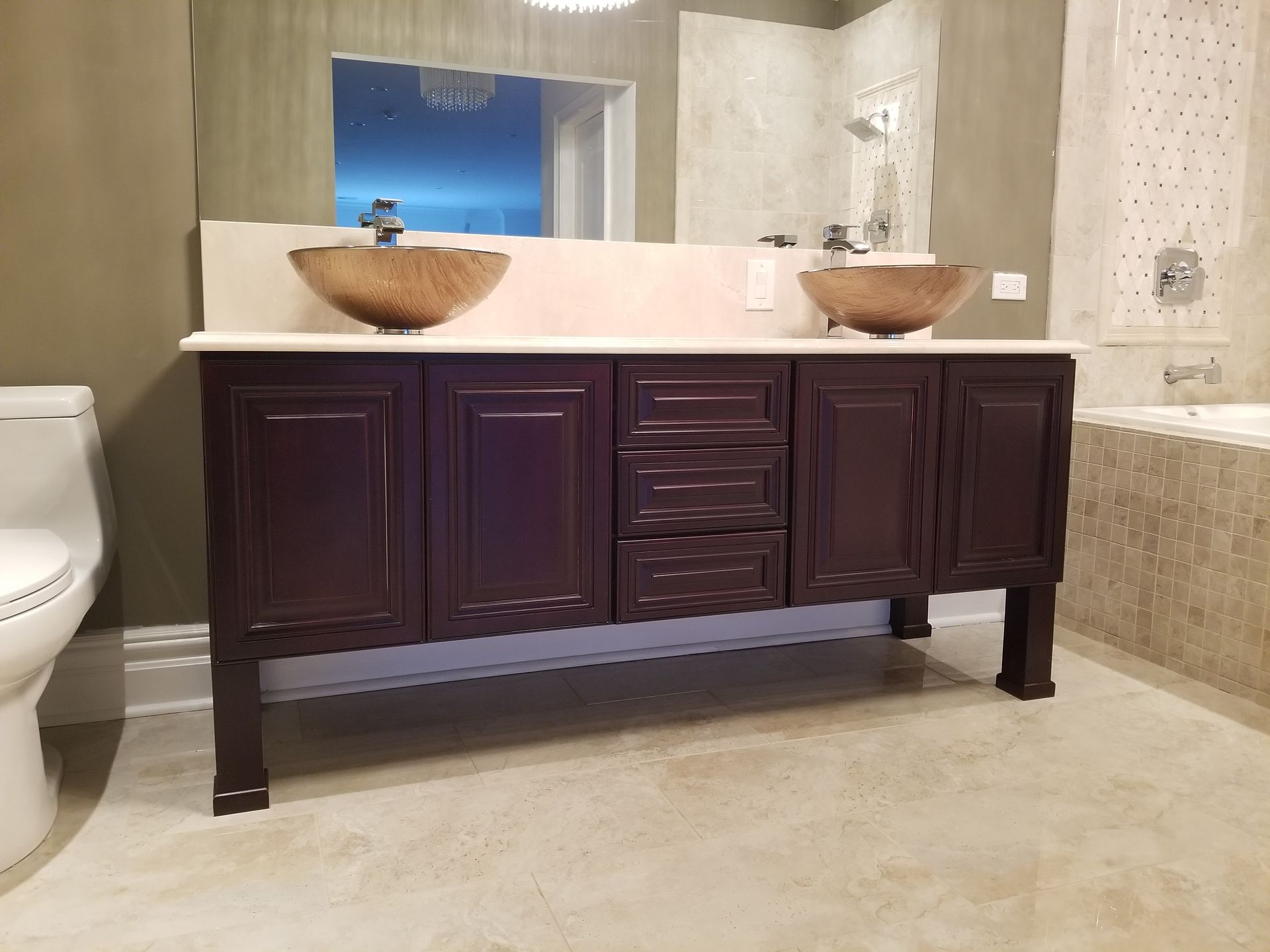 Dark wood double vanity with two vessel sinks in a beige tiled bathroom