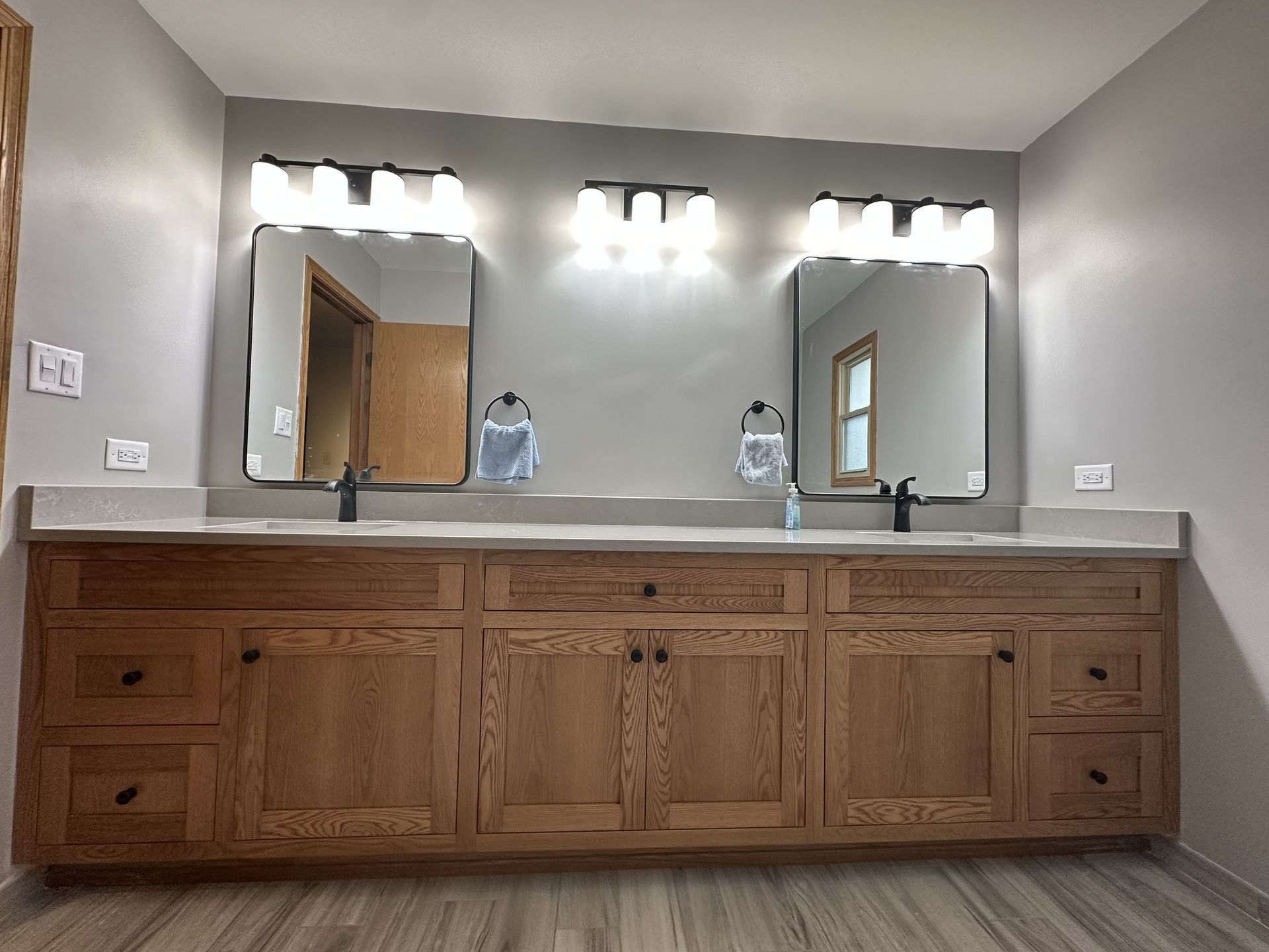 Modern bathroom with double vanity, large mirrors, and wood cabinets under bright vanity lights
