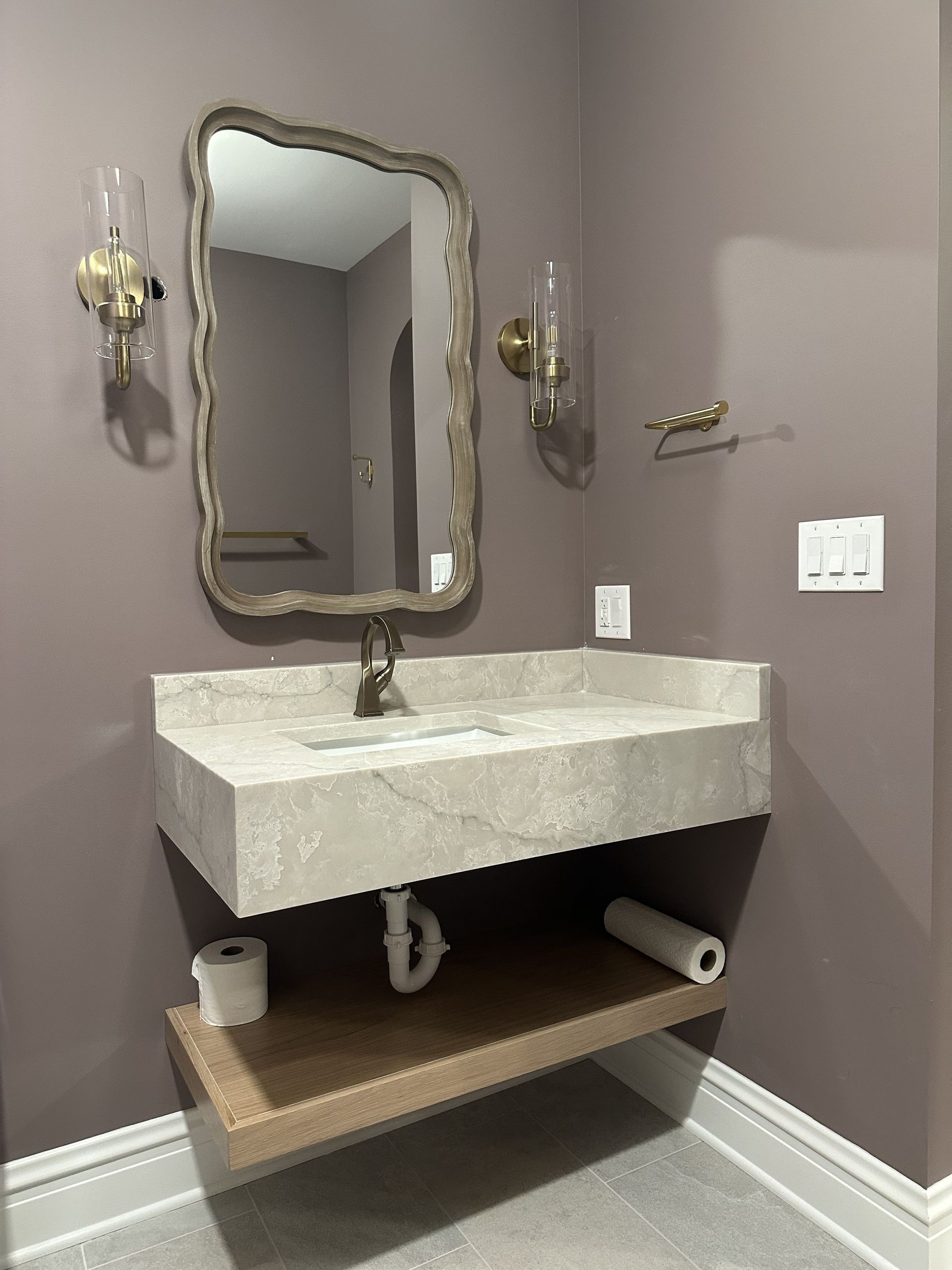 Bathroom vanity with stone sink, ornate mirror, wall sconces, and open shelf beneath.
