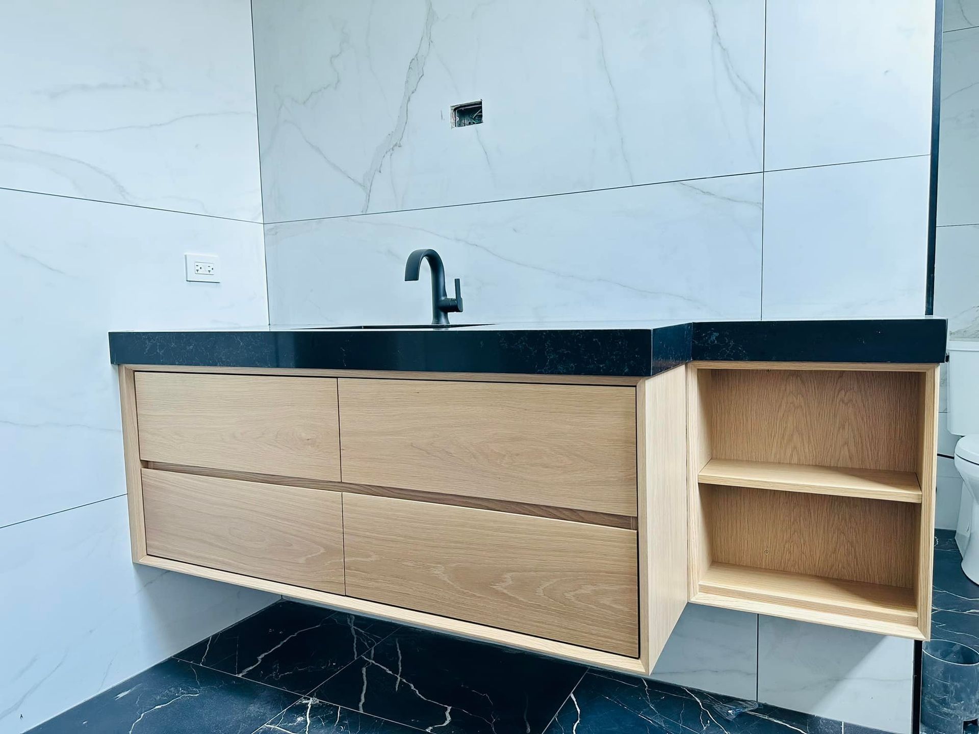 Modern kitchen sink cabinet with black countertop, wood finish, and open side shelves against tiled walls