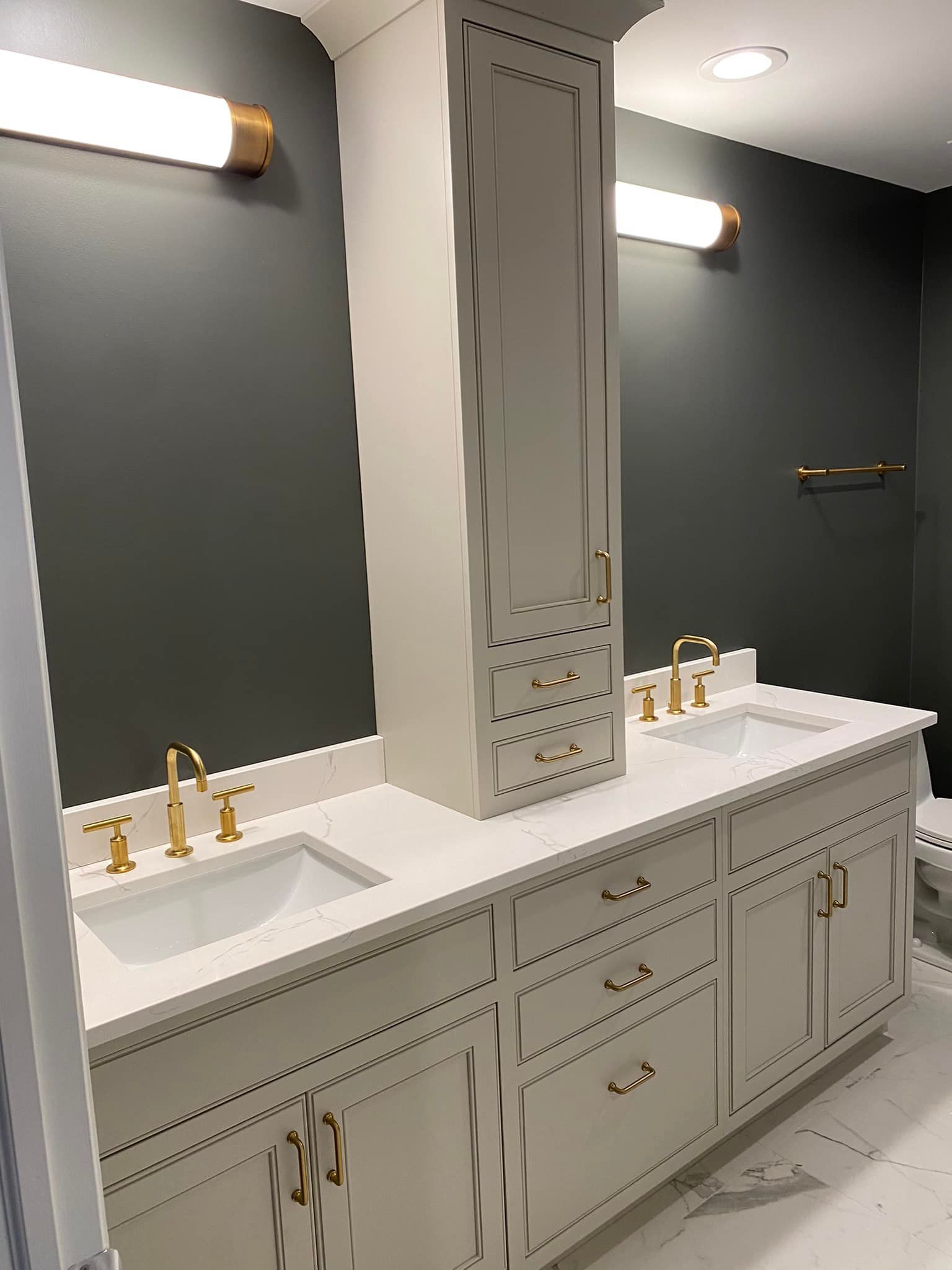 Elegant bathroom vanity with double sinks, gold fixtures, and a large mirror on dark walls