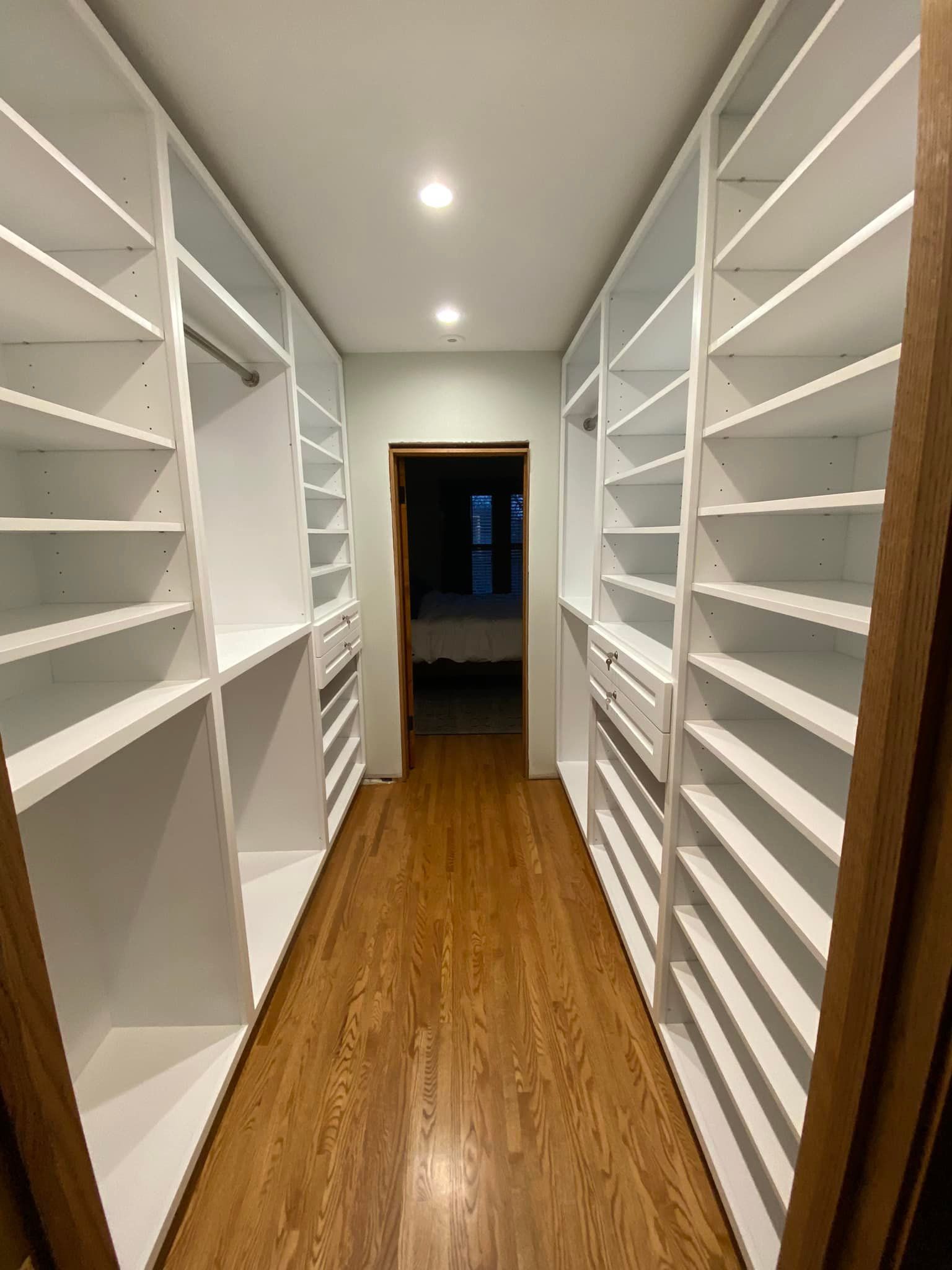 Narrow white walk-in closet with built-in shelves on both sides and wood flooring