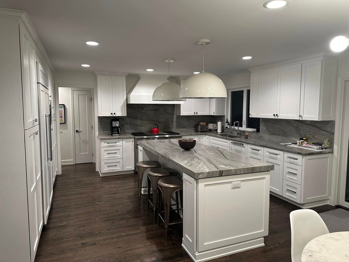 Bright modern kitchen with white cabinets, granite island, dark wood floors, and recessed ceiling lights