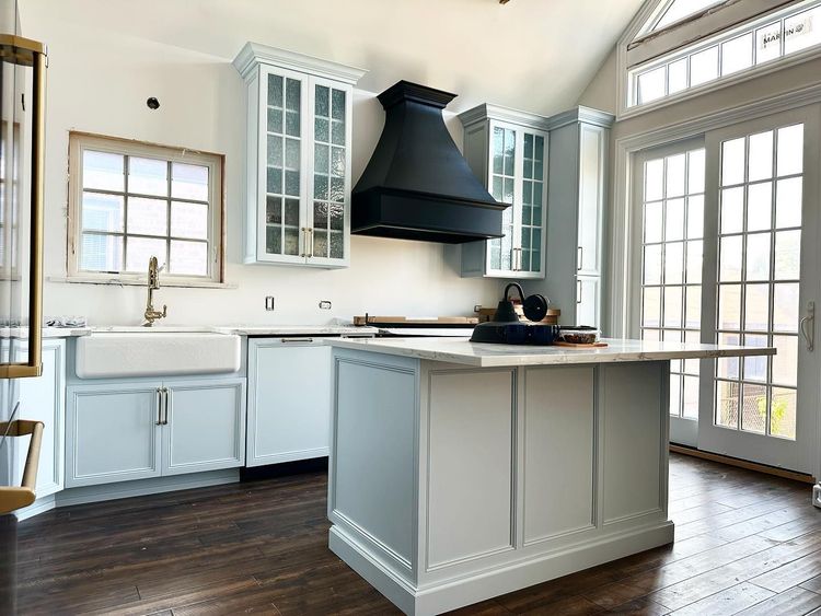 Bright white kitchen with island, black range hood, glass cabinets, and French doors.