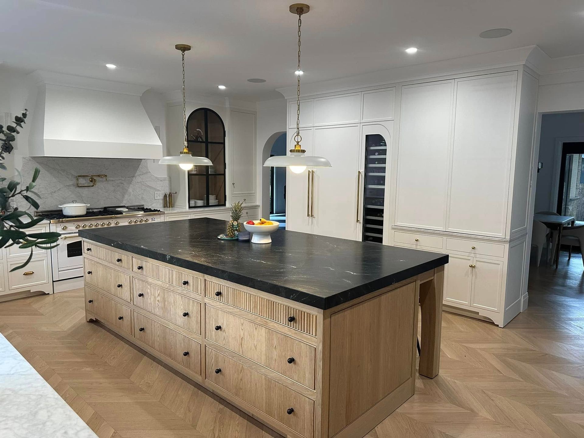 Modern kitchen with large black island, pendant lights, white cabinets, and herringbone wood floors
