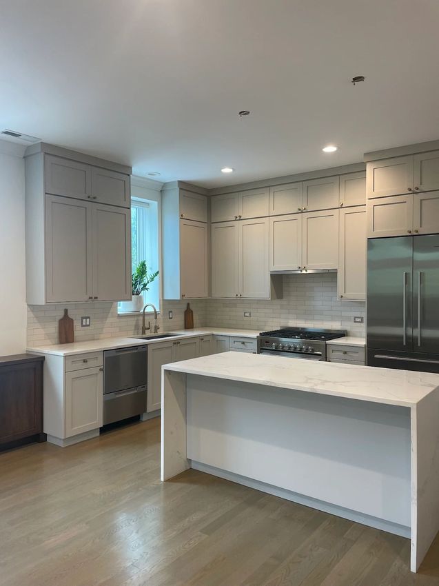 Bright modern kitchen with white cabinets, stainless appliances, and a white island on wood flooring