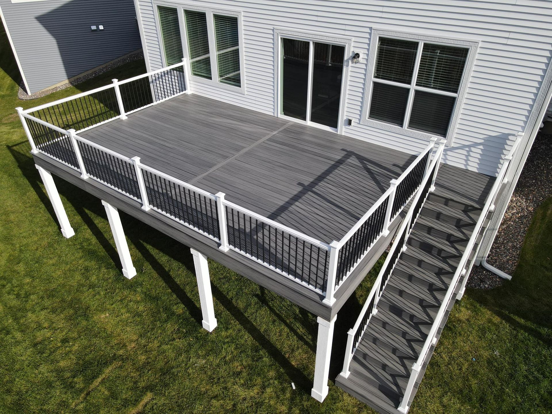 An elevated, rectangular gray composite deck with white railings and stairs, attached to a house with white siding.
