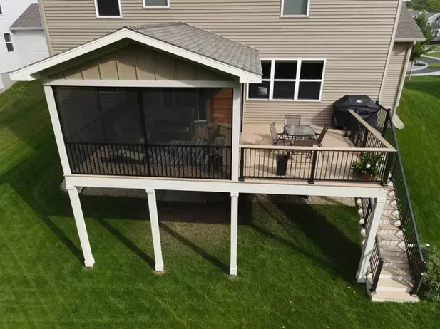 An elevated deck with a screened porch and open-air seating area attached to the back of a beige, two-story house.