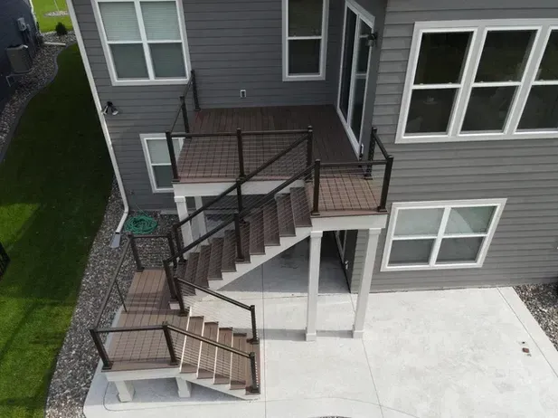 An elevated composite deck with black railings and a two-flight staircase leading down to a concrete patio.