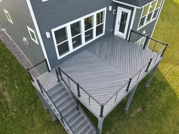 High-angle shot of a gray composite deck with a diagonal pattern, black railing, and stairs leading to a grassy lawn.
