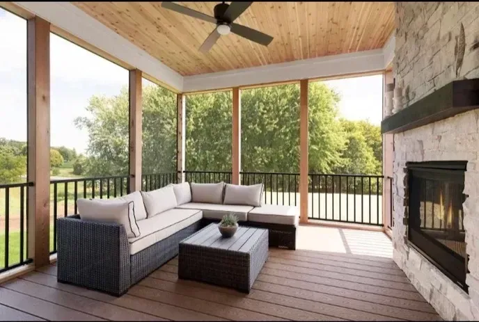 Screened-in porch with a stone fireplace, dark wicker sectional sofa, coffee table, wood ceiling, and outdoor view.