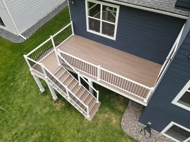 An elevated tan deck with white railings and stairs attached to a dark blue house, overlooking a green lawn.