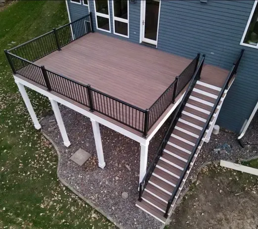 An elevated brown composite deck with black metal railings and a staircase leading down to a landscaped yard.