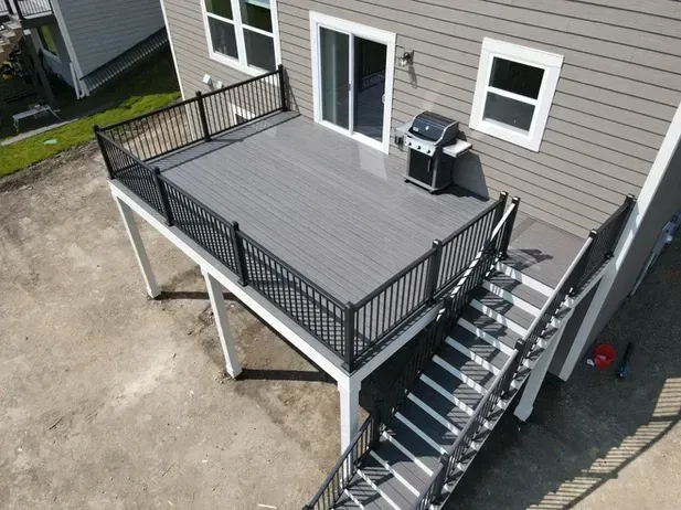 An elevated gray composite deck with black railings and stairs, attached to the back of a house with tan siding.