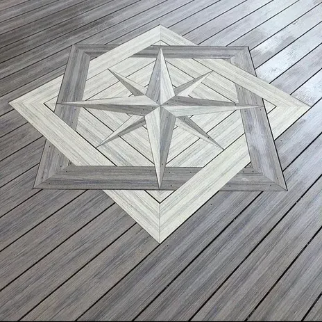 A compass rose inlay made of light and dark gray wooden decking planks, set into a larger gray wood deck surface.