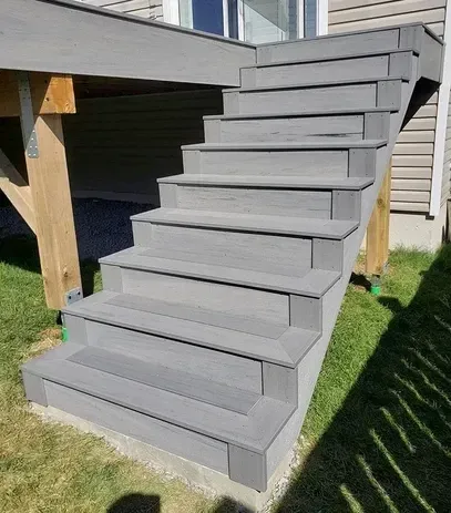 A set of grey composite deck stairs leading up to a house exterior, built over a grass lawn.