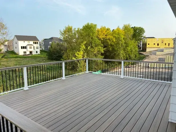 A spacious, elevated composite deck with black metal railings overlooking a backyard with trees and nearby houses.
