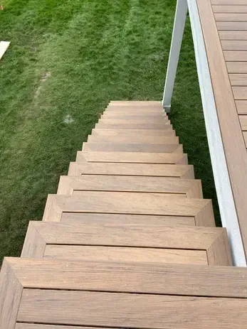 A top-down view of light-brown wooden deck stairs descending to a grassy yard.