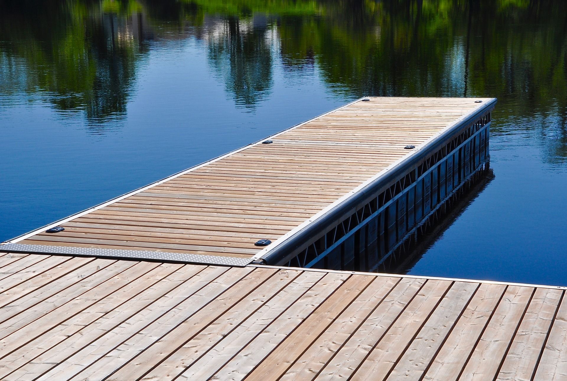A wooden dock extending into calm blue water, with a textured patterned platform at its end.