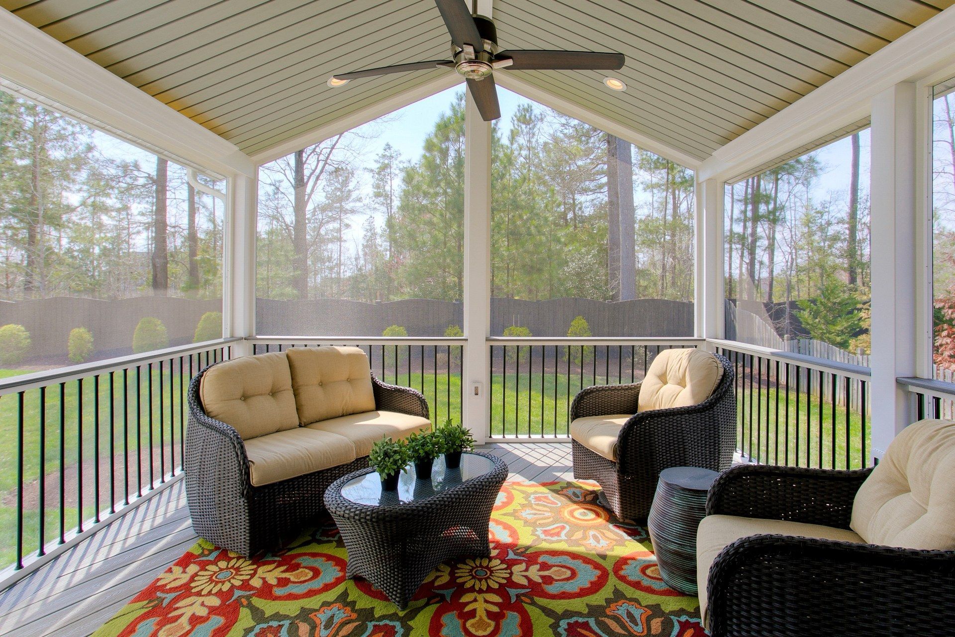A screened-in porch with a wicker sofa, two matching armchairs, a coffee table, and a colorful patterned rug.