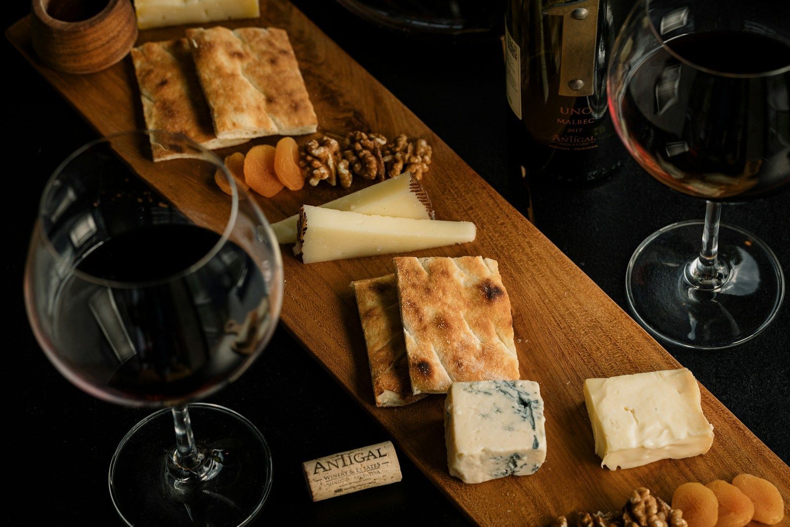 A cheese board with brie, blue cheese and crackers beside glasses of red wine