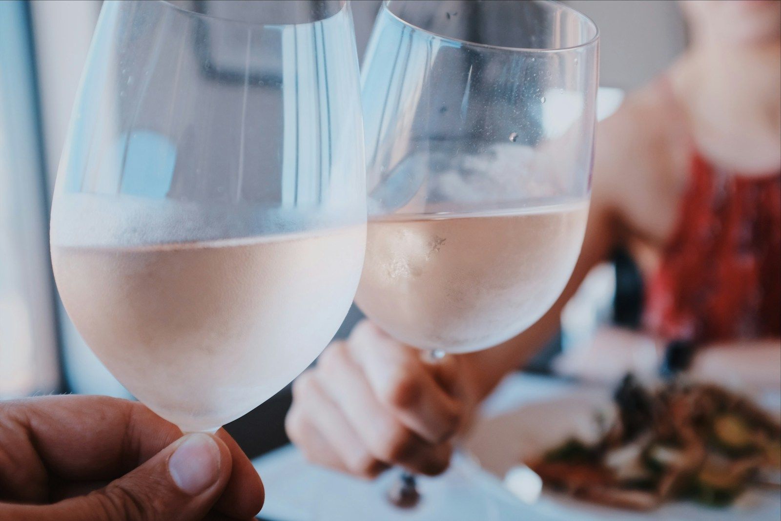 Two glasses of rosé raised in a toast over a table of small plates