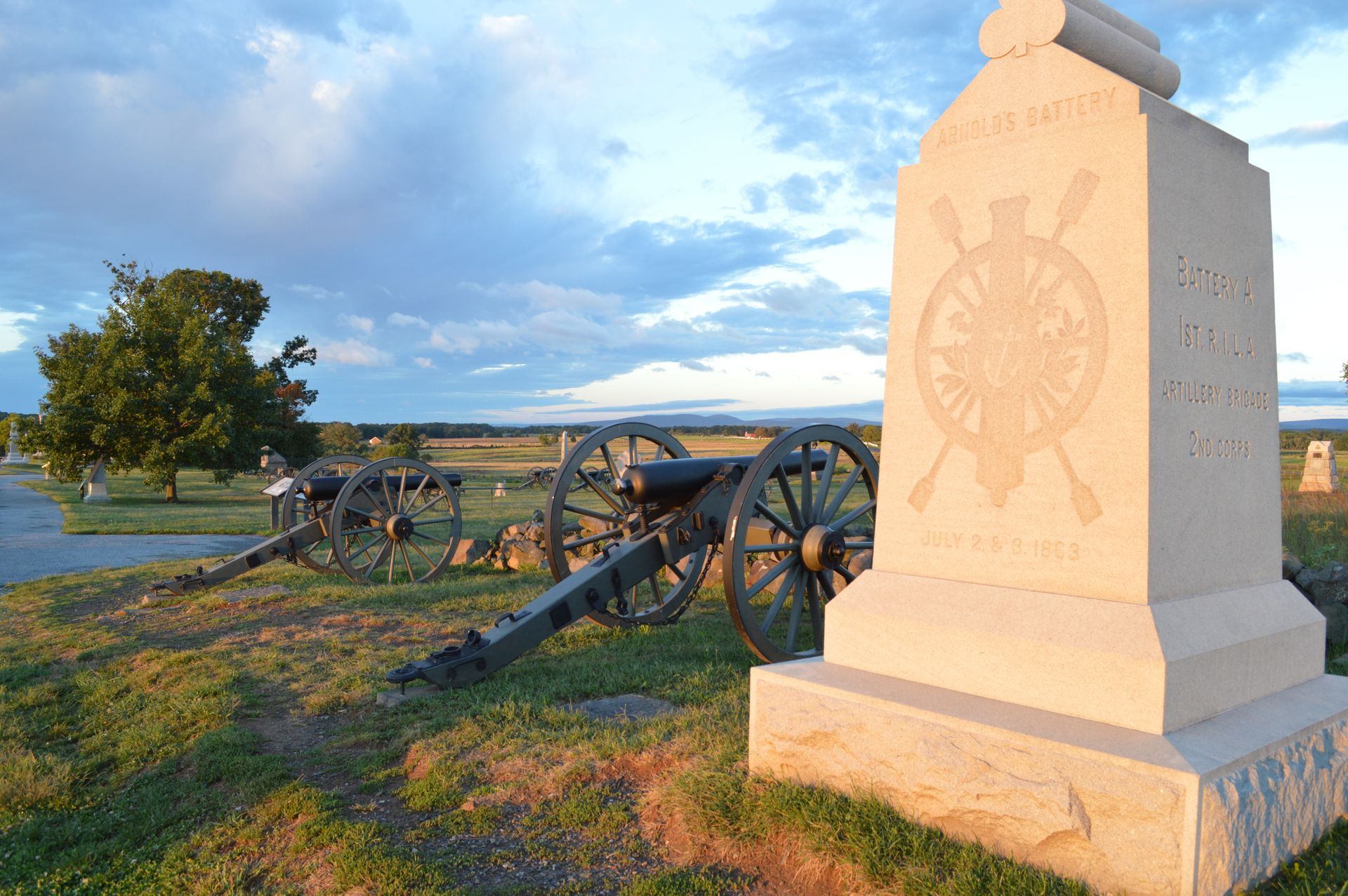Civil War cannon and stone monument at sunset in a grassy field near water