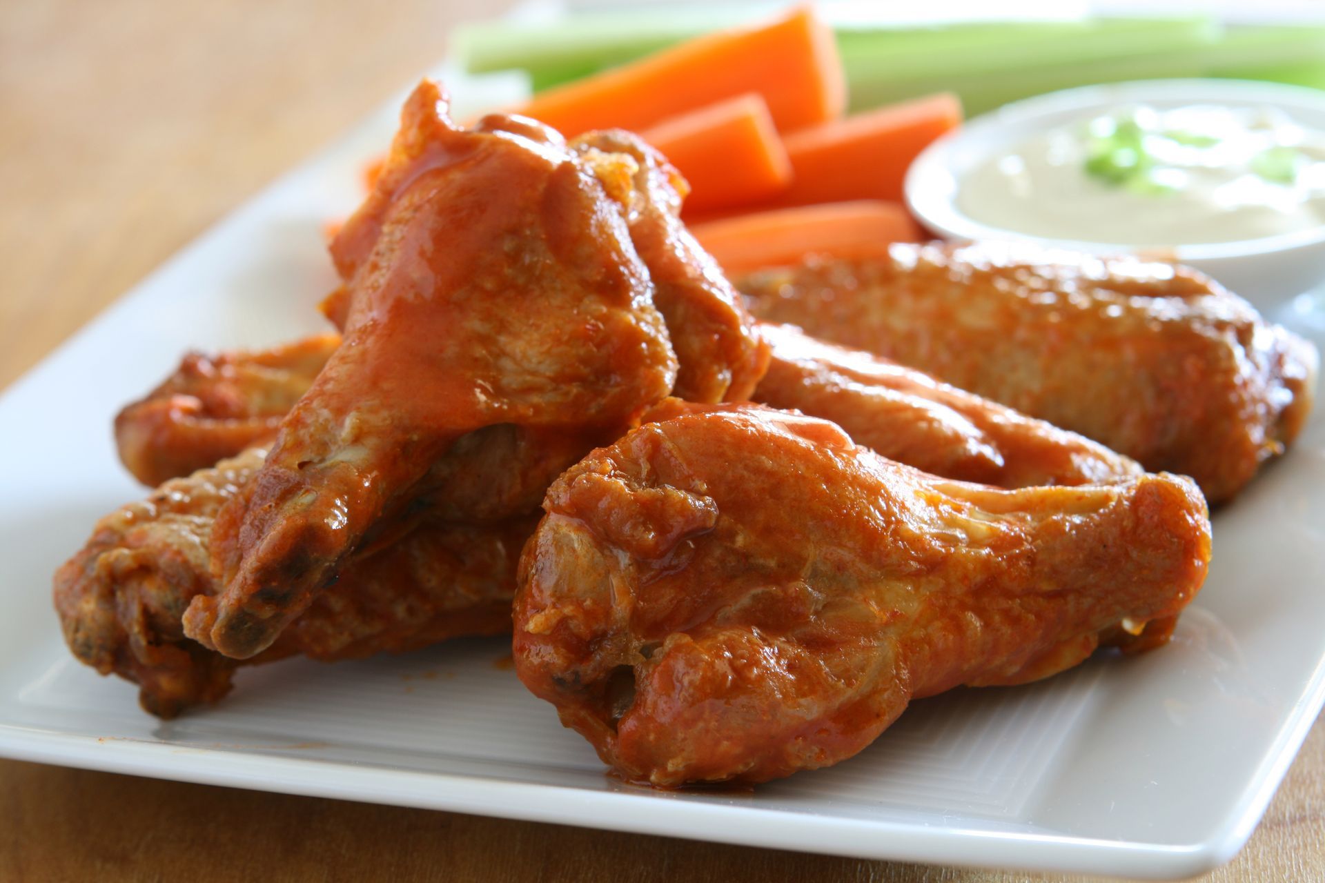 Plate of glazed chicken wings with carrot sticks and ranch dip