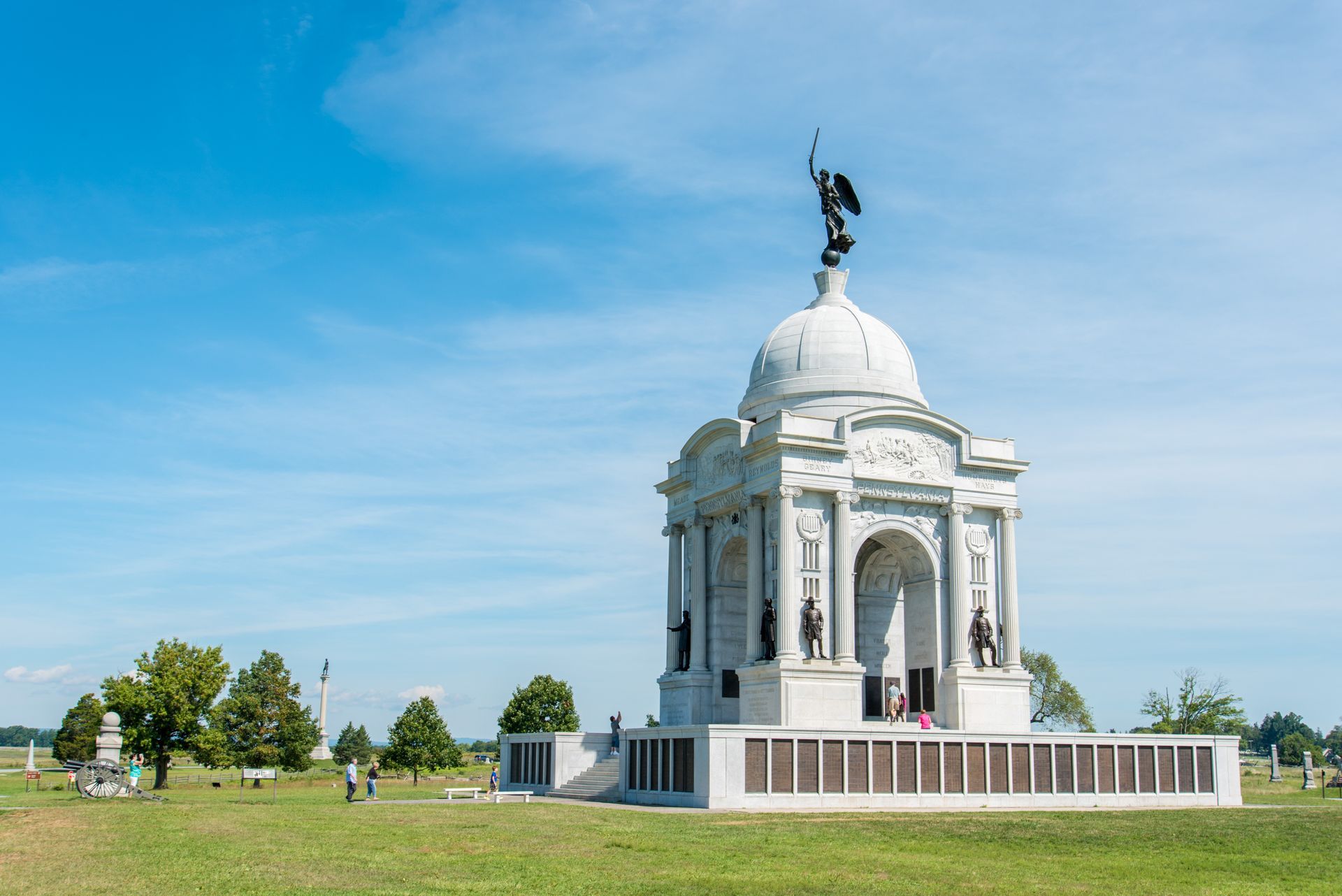 White memorial pavilion with statue on a grassy field under a blue sky