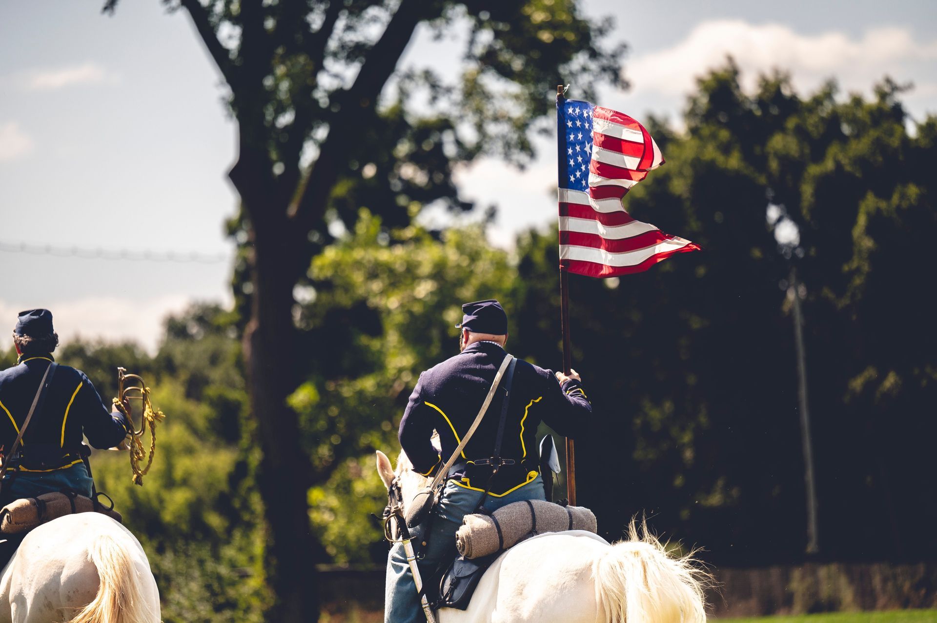 Mounted riders holding an American flag in a wooded outdoor setting