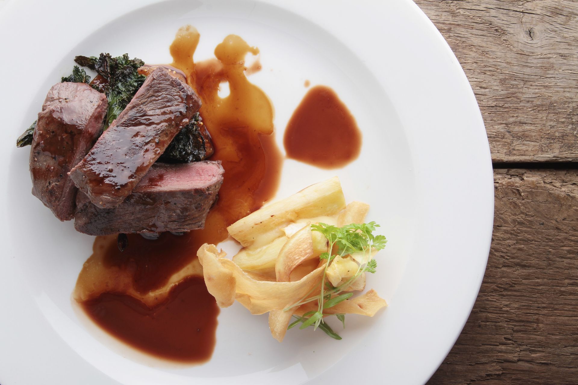Plated steak with sauce and sautéed vegetables on a white dish