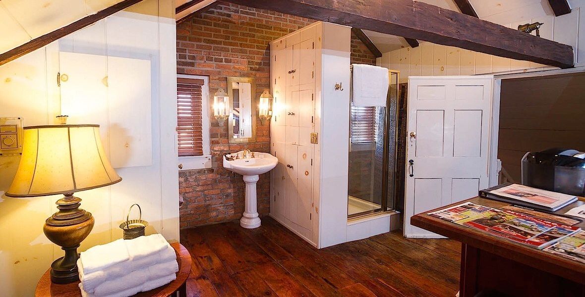 Cozy rustic room with exposed beams, white closet doors, sink, and lamp-lit side table