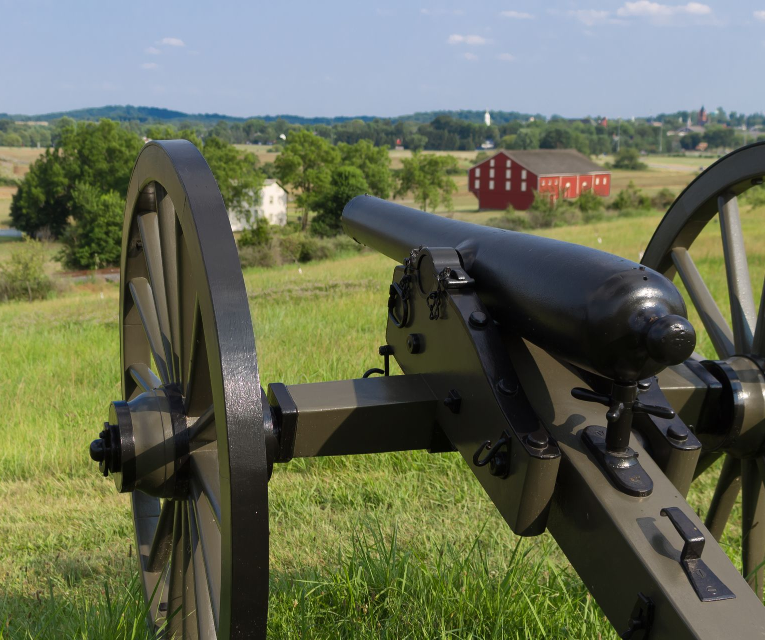Historic cannon in a grassy field overlooking a rural landscape with red barns in the distance