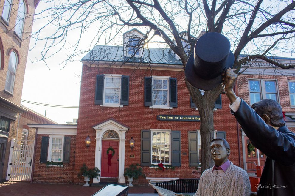 Red-brick house with a red door and large black hat sculpture in front of bare trees