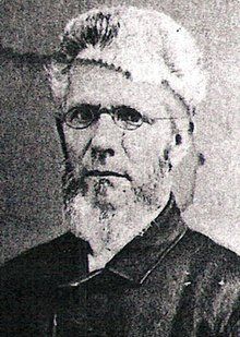 Black-and-white portrait of a bearded man wearing glasses and a fur hat, facing slightly left.