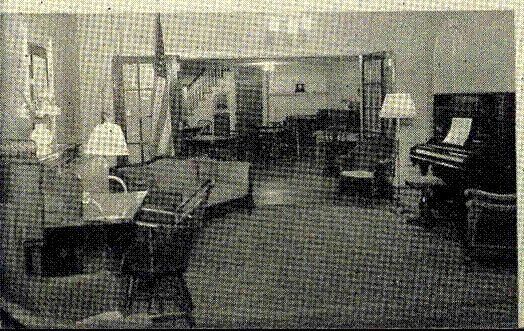 Dim living room with armchairs, lamps, and a piano in the background