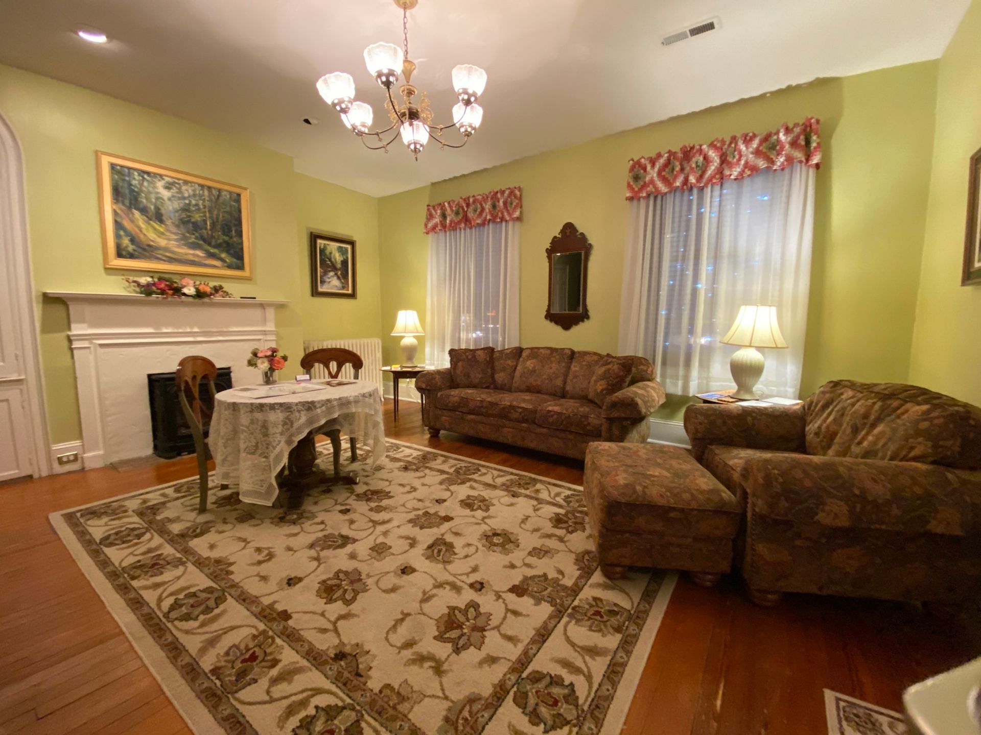 Elegant living room with floral rug, brown sofas, white table, fireplace, and window valances
