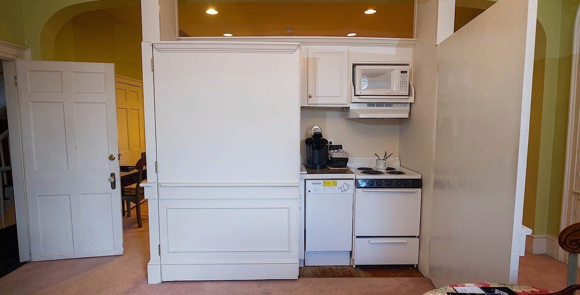 Small kitchen nook with white cabinets, stove, microwave, and a white door in the background.