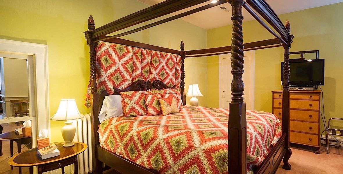 Four-poster bed with red quilt in a cozy bedroom, flanked by lamps and wooden furniture